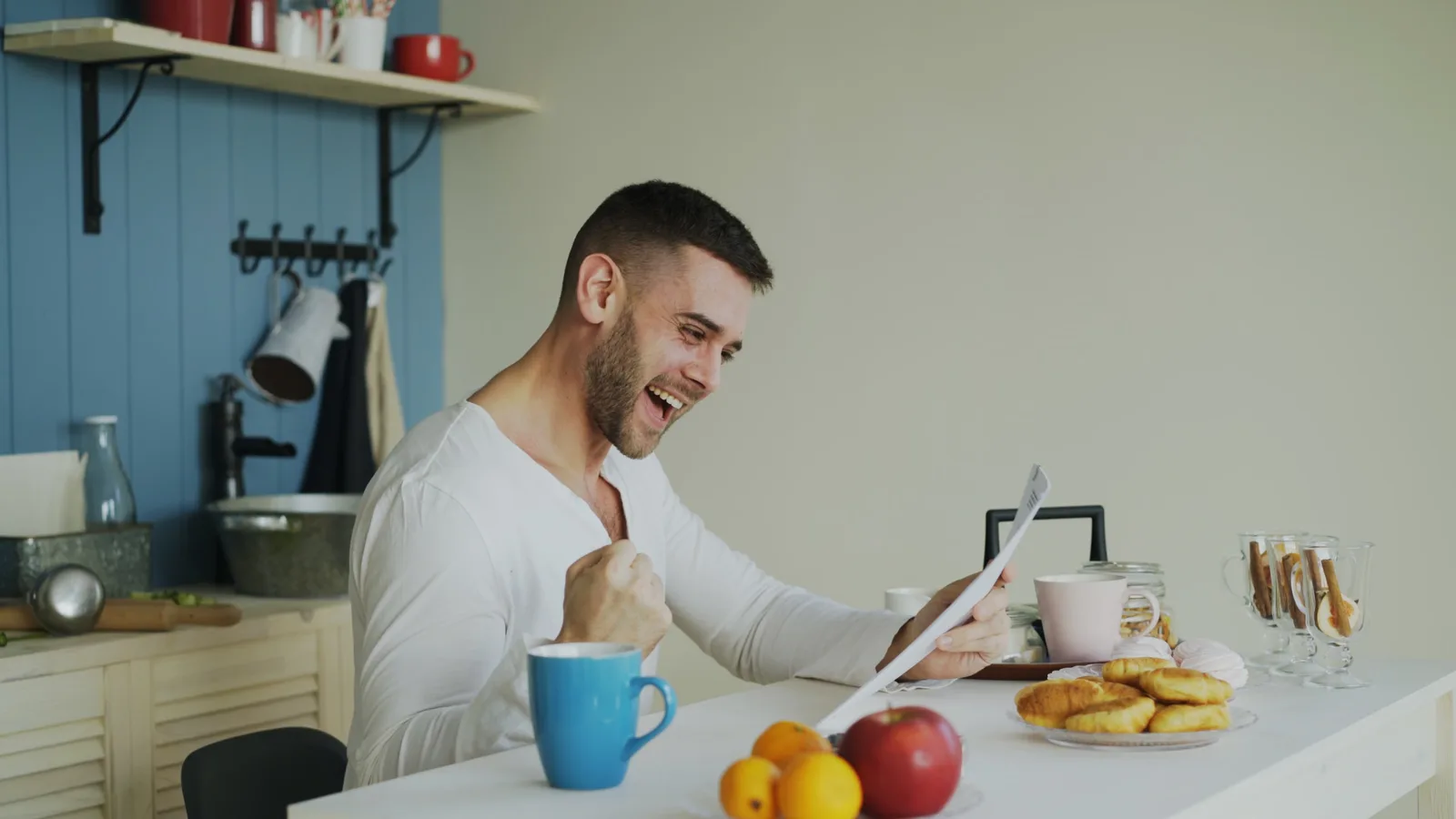 Excited man celebrating good news while having breakfast in a cozy kitchen.