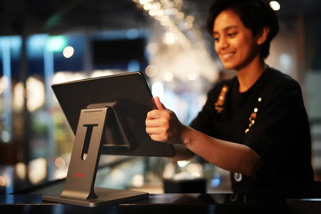 Smiling female cashier using a touchscreen in a modern restaurant setting. Mapping POS totals without losing refunds and fees
