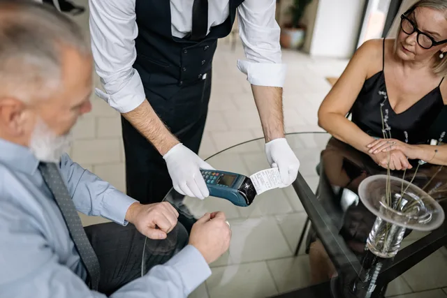 A couple making a contactless payment using a credit card at a restaurant table. Reconciling card transactions with submitted receipts